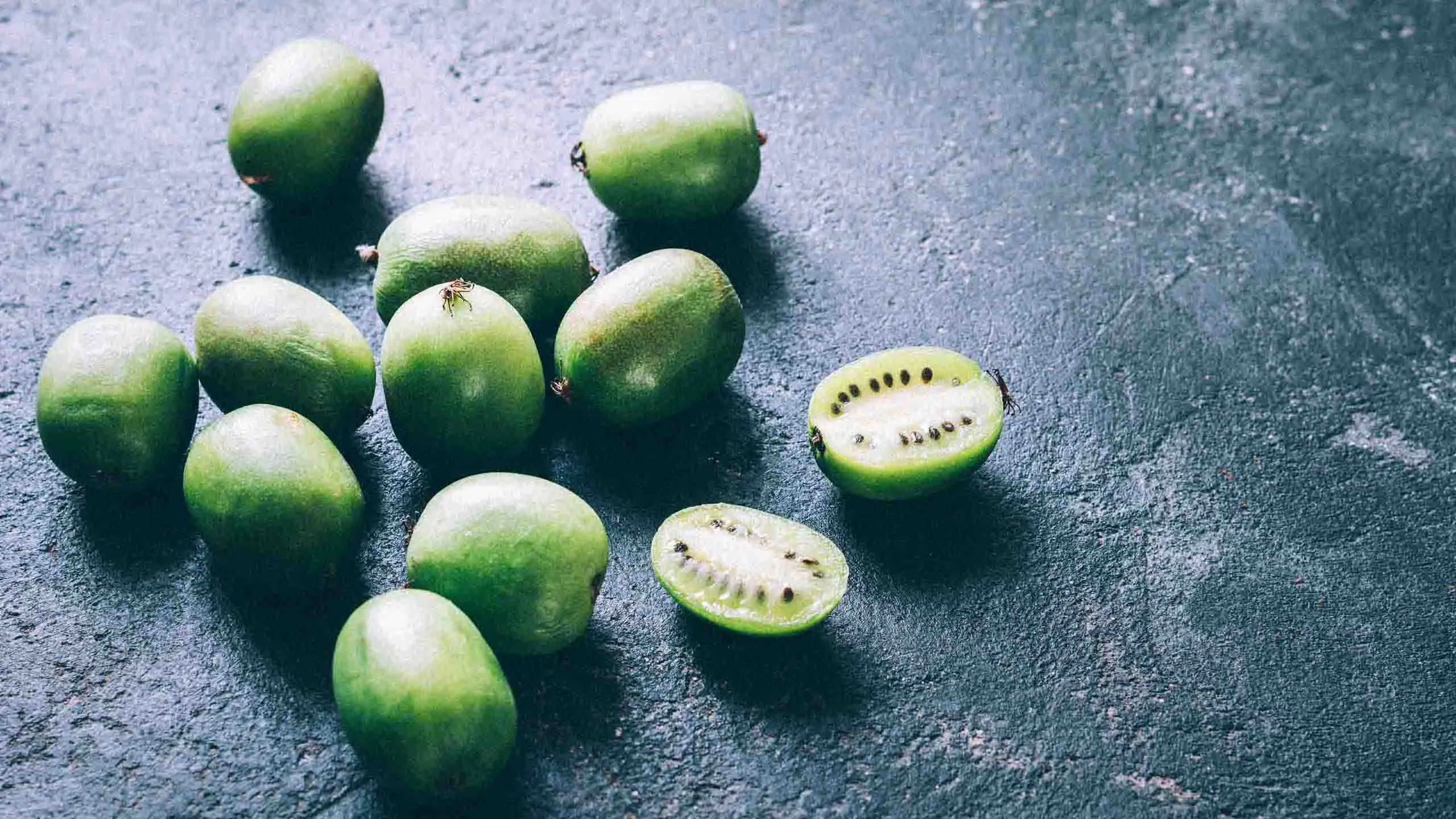 Kiwi Actinidia Sentyabraskaya i närbild visar de små, skalfria kiwibären – några hela och några delade – på en mörk yta.